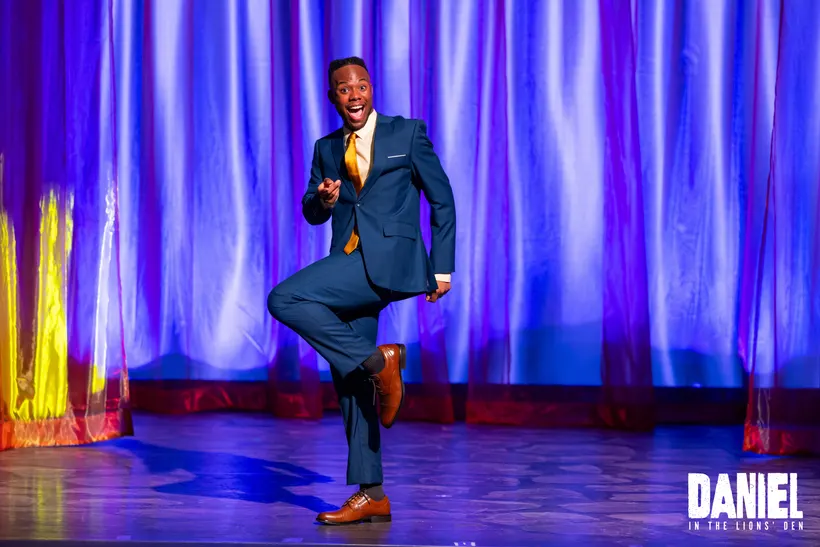The show's narrator, in a blue suit and gold tie, dances center stage
