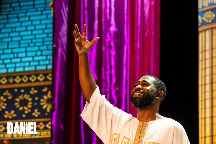 A performer in white raises a hand in praise before the palace curtains
