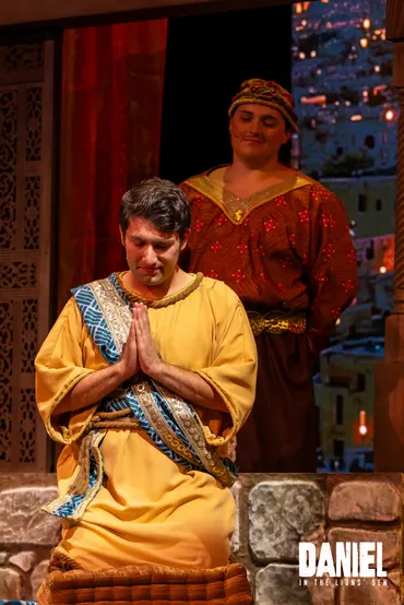 Daniel, in gold robes, prays as a palace official watches from behind