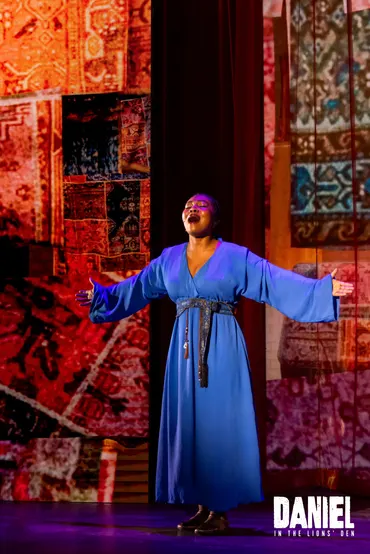 A performer sings beneath the glowing tapestries of the palace set